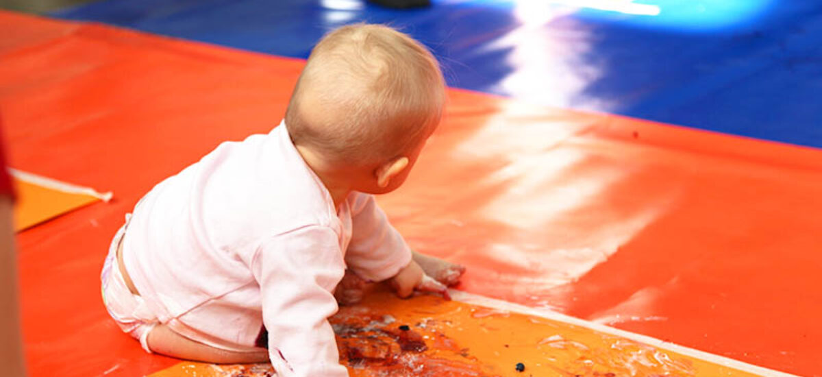 Vauva istuu värikkäällä lattialla. Tekee värikylpy-taidetta marjoilla ja jauheella.