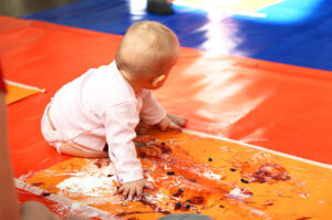 Vauva istuu värikkäällä lattialla. Tekee värikylpy-taidetta marjoilla ja jauheella.