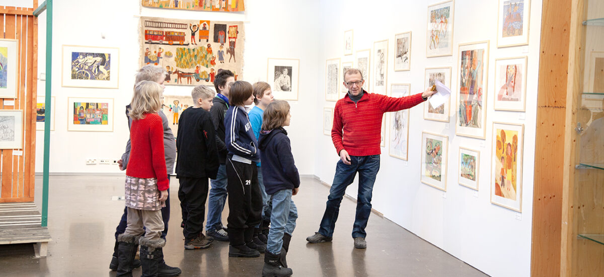 Galleriatilassa opas esittelee seinällä olevia teoksia lapsiryhmälle. Opastukset